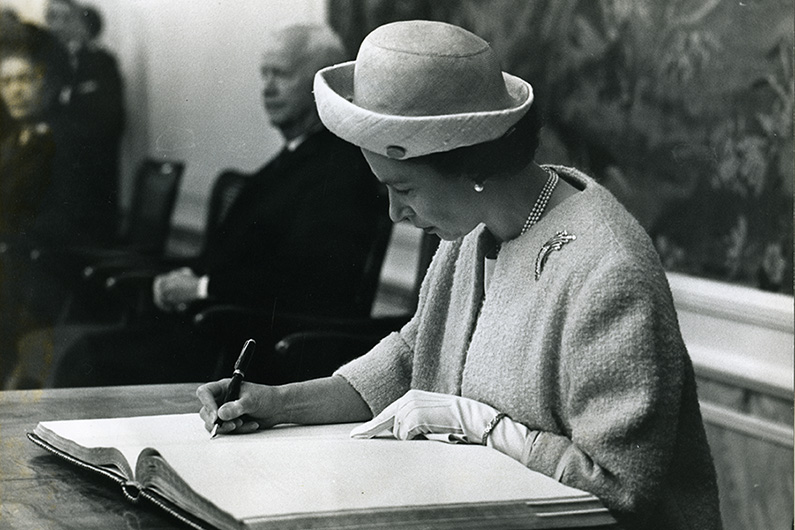 Schwarzweiß-Fotografie von Queen Elizabeth II., die sich im Alten Rathaus am Marktplatz ins Goldene Buch der Stadt Bonn einträgt
