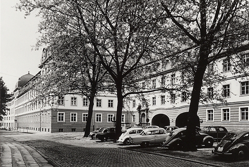 Hinter Bäumen und mehreren Autos ist das alte Stadthaus in einer Aufnahme von 1962 zu sehen.