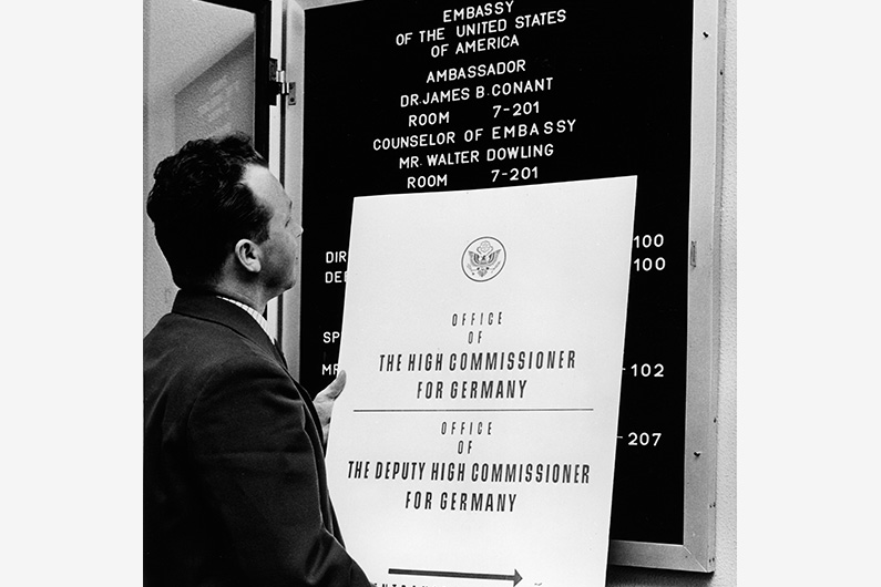 Black and white photography, a man exchanges the information board of the US-American High Commissariat for one with the imprint "Embassy of the United States of America".