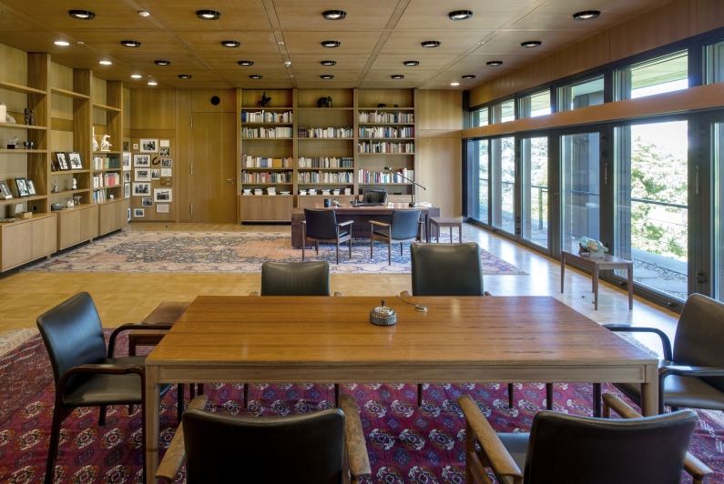 Wood-panelled study with desk and conference table, shelving and wide window front