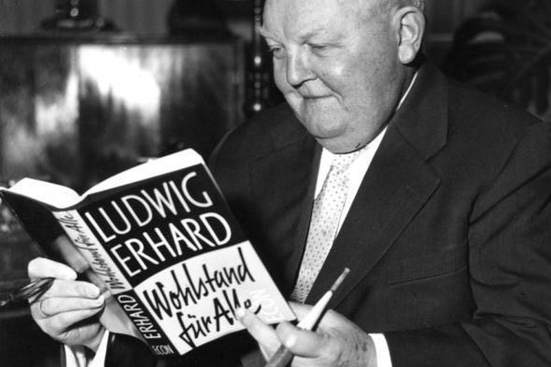 Black and white photograph by Ludwig Erhard, who is leafing through his book in his office.