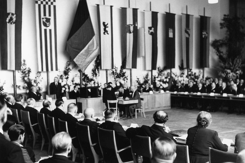 Black and white photography, plenary hall with lectern and members of the Bundesrat, on the wall the flags of the federal states of Germany.