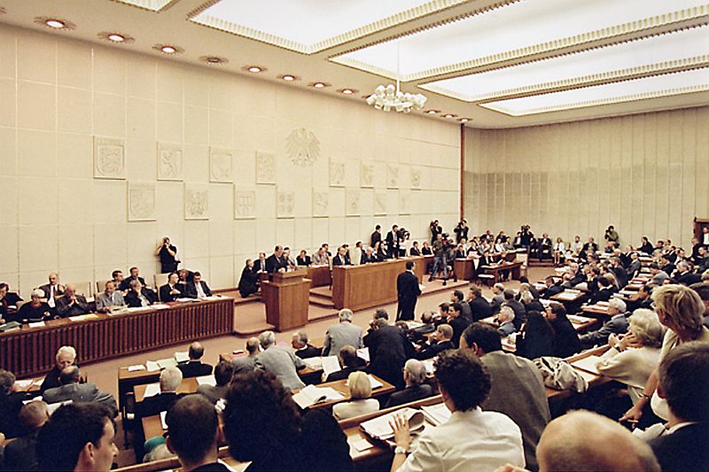 Fully manned plenary hall of the Bundesrat meeting, in front of the wall a a lectern, behind of it the 16 coats of arms of the federal states of Germany.