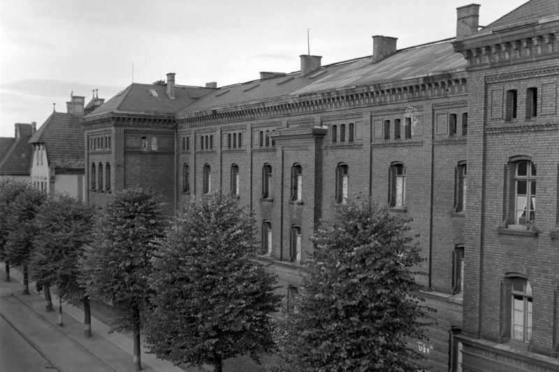 Schwarzweiß-Fotografie der Bonner Ermekeilkaserne, Backsteingebäude im "normannischen Stil", davor eine Straße mit Baumallee