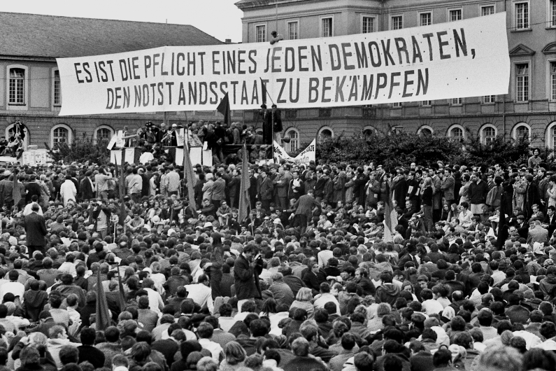 Demonstranten versammeln sich vor dem Universitätsgebäude im Bonner Hofgarten, über ihren Köpfen ein großes Plakat mit der Aufschrift "Es ist die Pflicht eines jeden Demokraten, den Notstandstaat zu bekämpfen"