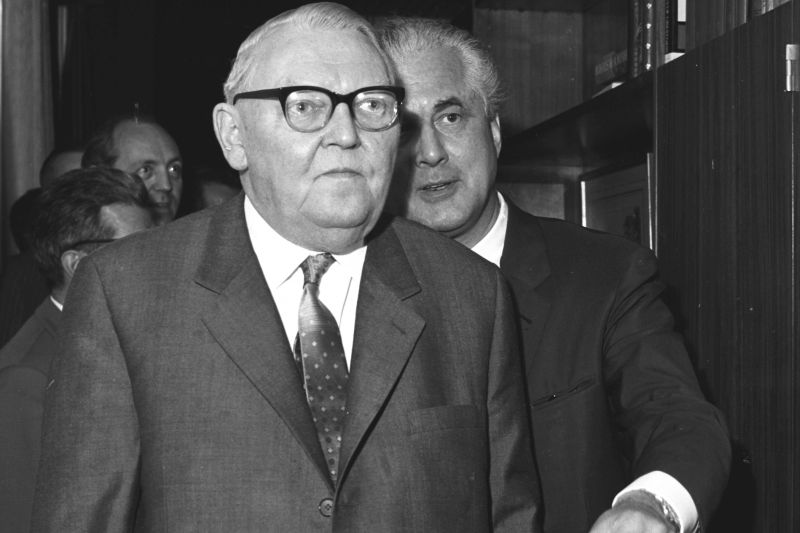 Black-and-white photography, close-up of concentrated Ludwig Erhard, Sep Ruf left behind him talking over his shoulder.