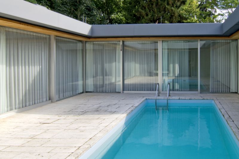 Small swimming pool in the courtyard of a bungalow with glazed walls.