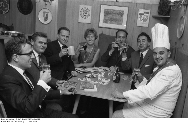  Seven people around a table with beer and wine glasses, cheering to the photographer