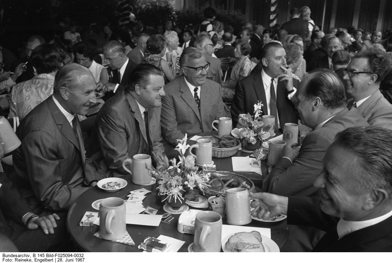 Several people sitting at tables, enjoying beer and pretzels