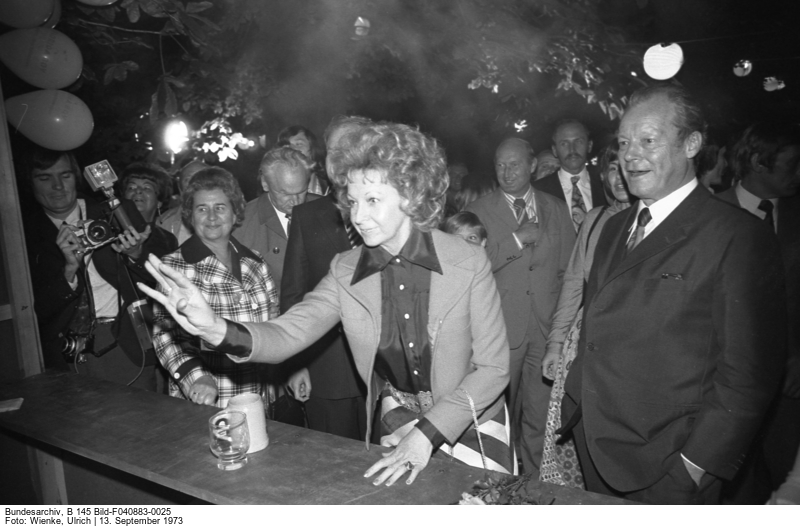 Schwarzweiß-Fotografie, zentral im Bild Willy Brandt und seine Ehefrau Rut beim Besuch eines Laubenpieperfests, dahinter weitere Gäste der Landesvertretung Berlin.