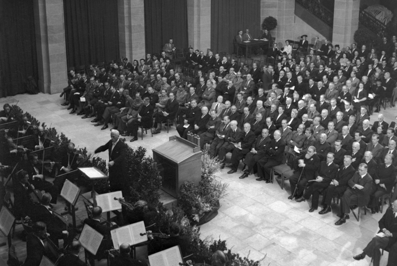 View of an orchestra with a conductor, in the background the audience.