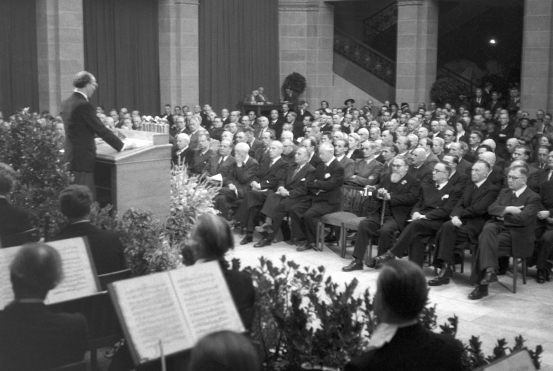 Black and white photograph, Karl Arnold (left) giving a speech to the Parliamentary Council (right side), in front of him an orchestra.