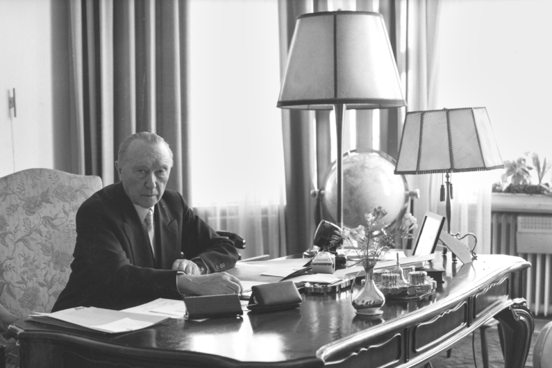 Black and white photography, Konrad Adenauer sits at his desk and looks into the camera.