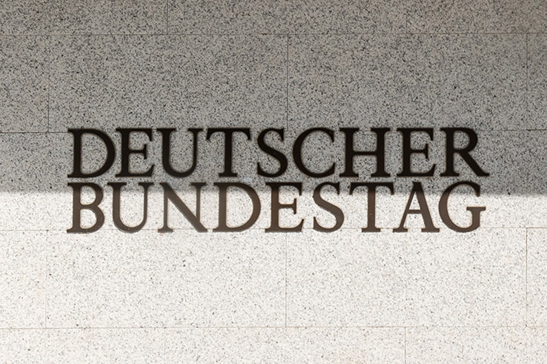 Blick auf eine sandsteinfarbene Außenwand mit schwarzem Schriftzug "Deutscher Bundestag"