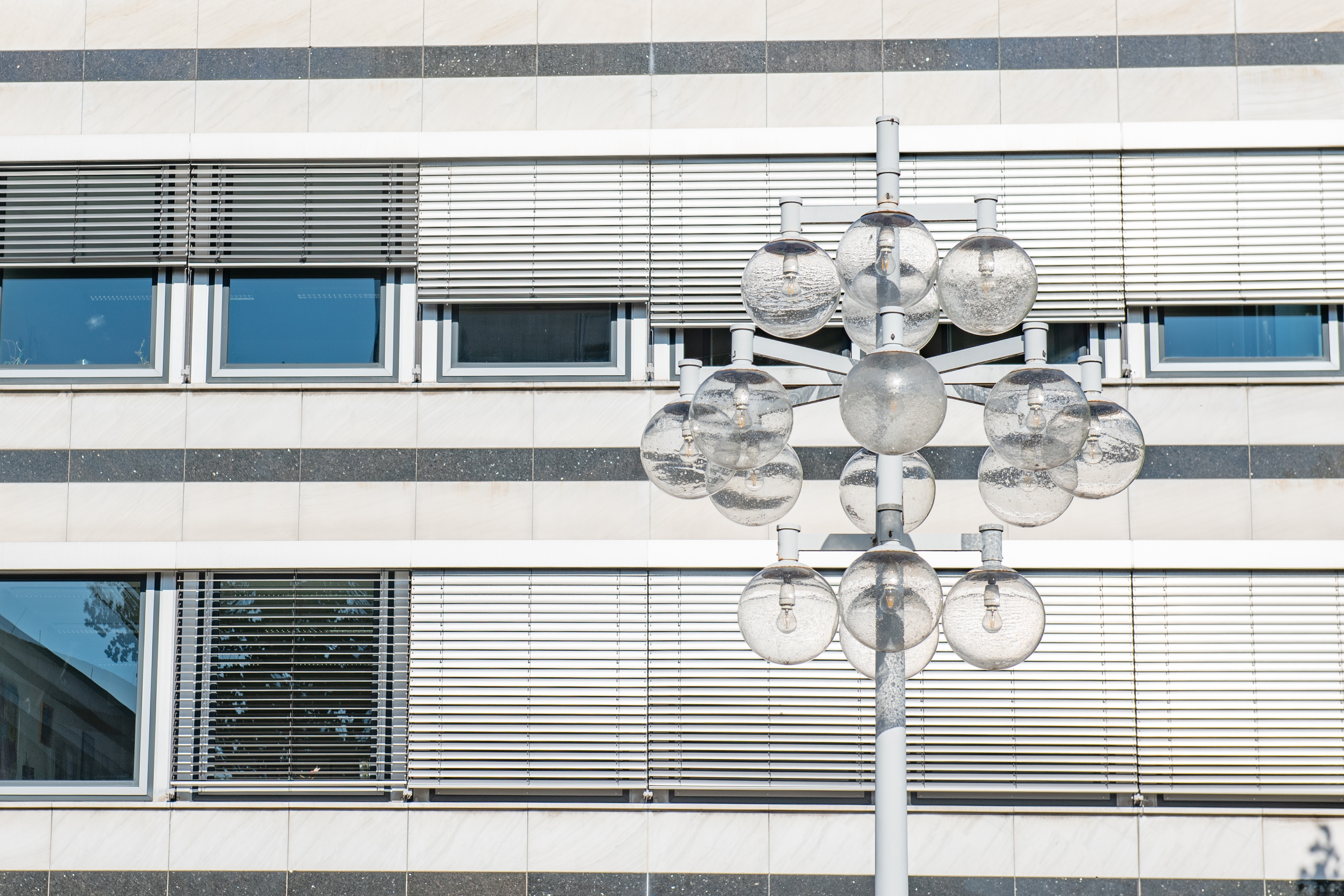 Office window with blinds, in front of it a striking street light with numerous round glass lights.