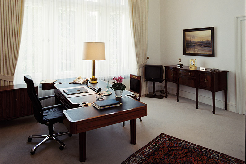 stylish room with a dark wooden desk, a carpet and a chest of drawers overlooking a large window.