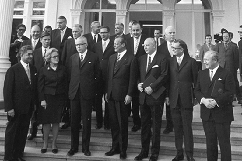 Black and white photography, a group of men in suits standing on the steps of a white building.